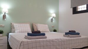 A neatly made double bed with a grid-patterned bedspread, two wall-mounted lamps, a small potted plant, and a window with a view.