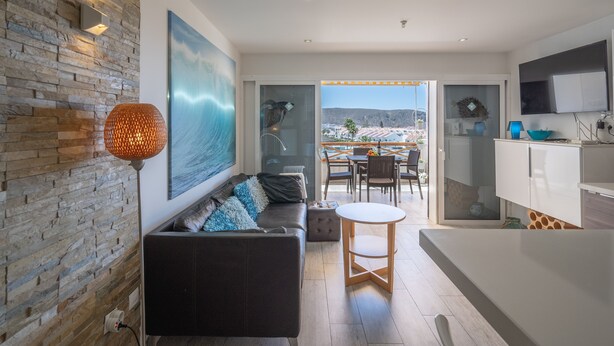 A modern living room with a stone wall, a large painting, a black sofa, and a round table. - GO2TENERIFE Apart'Cala Pool & Beach at 5 mins (Arona)