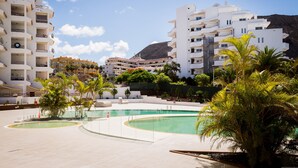 A resort with a swimming pool, multiple white buildings, and palm trees. - GO2TENERIFE Apart'Cala Pool & Beach at 5 mins (Arona)