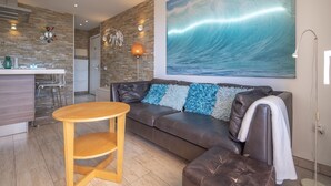 A modern living room with a brown leather sofa, a wooden coffee table, and a large wave painting on the wall. - GO2TENERIFE Apart'Cala Pool & Beach at 5 mins (Arona)