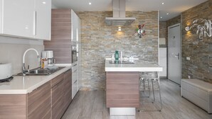 A modern kitchen with a stone backsplash, wooden cabinets, and a central island with bar stools. - GO2TENERIFE Apart'Cala Pool & Beach at 5 mins (Arona)