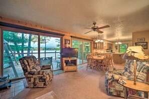 A cozy living room with a television, wooden furniture, and large windows overlooking a deck. - Cozy Hayward Cottage w/ Dock & Lakefront View (Hayward)