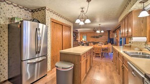 A kitchen with wooden cabinets, a stainless steel refrigerator, a wooden dining table with chairs, and a trash can. - Cozy Hayward Cottage w/ Dock & Lakefront View (Hayward)