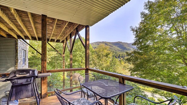 Une terrasse extérieure couverte, équipée d’un barbecue, d’une table et de chaises, et offrant une vue sur une zone boisée.