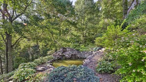 Un jardin paisible avec un petit étang, entouré d’une végétation luxuriante et surmonté d’un pont de pierre.