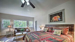 Une chambre spacieuse avec un grand lit, un ventilateur de plafond et une vue sur l’extérieur grâce à de grandes fenêtres.