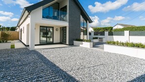 A modern two-story house with a large glass window, a gravel driveway, and a white exterior. - Gwel y Wyddfa - sleeps 6 guests in 3 bedrooms (Rhosneigr)