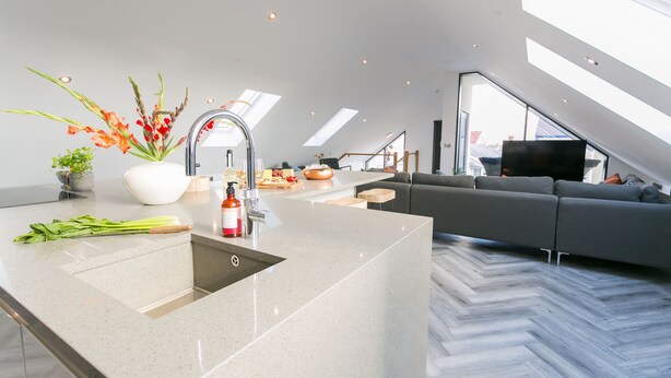 A modern kitchen with a central island, a grey sofa, and a large window. - Gwel y Wyddfa - sleeps 6 guests in 3 bedrooms (Rhosneigr)