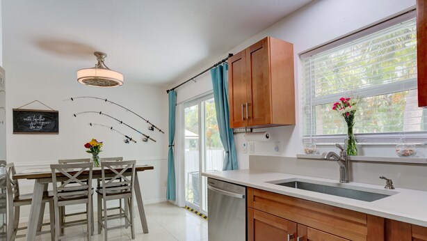 A modern kitchen with wooden cabinets, a white countertop, a built-in dishwasher, and a window with curtains. - Steps to the water! 🏝️  (West Palm Beach)