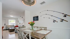 A dining area with a wooden table and chairs, a vase with flowers, and fishing rods on the wall. - Steps to the water! 🏝️  (West Palm Beach)