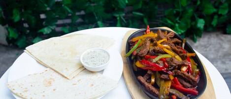 A plate of flatbread, a bowl of sauce, and a skillet with beef and bell peppers.