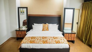 Une chambre d’hôtel avec un grand lit, deux tables de chevet, un miroir, un téléphone et un rideau.