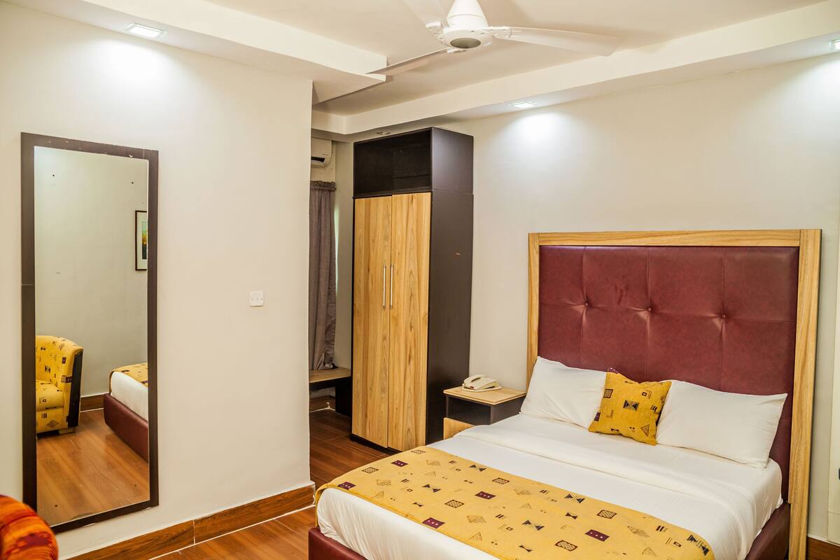Habitación de hotel con una cama grande, un armario, una mesita de noche con teléfono y un espejo.