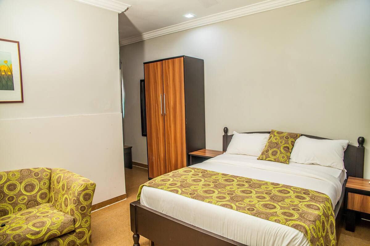 Una habitación de hotel con una cama, un armario de madera, una silla y una mesita de noche.