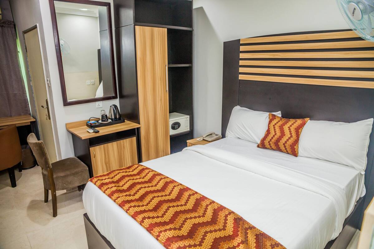 Una habitación de hotel con cama, escritorio, silla, armario y espejo.
