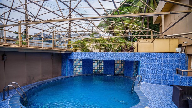Une piscine intérieure aux murs recouverts de mosaïques bleues, dotée d’un escalier en métal et d’une structure de plafond en verre.