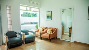 Un espace d’accueil comprenant un canapé, deux fauteuils, une porte vitrée et une vue sur l’extérieur.