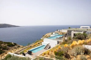 Una propiedad costera con piscina, mobiliario exterior y vista al mar.