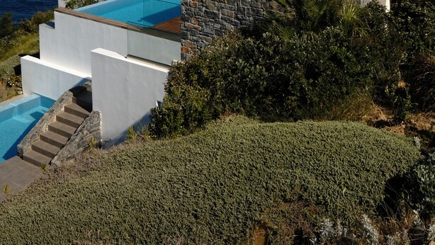 A modern villa with a pool, stone walls, and a view of the sea.