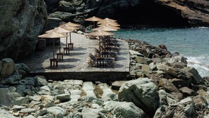 A rocky coastal area with a small seating area featuring umbrellas and chairs.