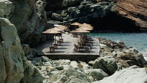 A rocky coastal area with a small outdoor seating area featuring tables and umbrellas.