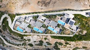 Vista aérea de um resort moderno com várias piscinas, painéis solares e uma estrada sinuosa.