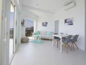 A modern living room with a white sofa, a dining table with chairs, and artwork on the walls. - Frontal beach view apartment with spacious balcony (Marbella)