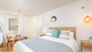Un dormitorio ordenado con una cama grande, una mesita de noche, una silla, un espejo y una lámpara colgante.