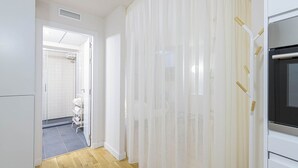 Un pasillo estrecho con suelo de madera, una puerta blanca que da al baño y una pared blanca con un respiradero.