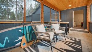 A wooden ceiling, two wicker chairs with cushions, a table, and a view of trees through large windows. - Bend Modern Cabin w/ Private Hot Tub . Fenced Yard, Game Room, Pet-Friendly (Bend)