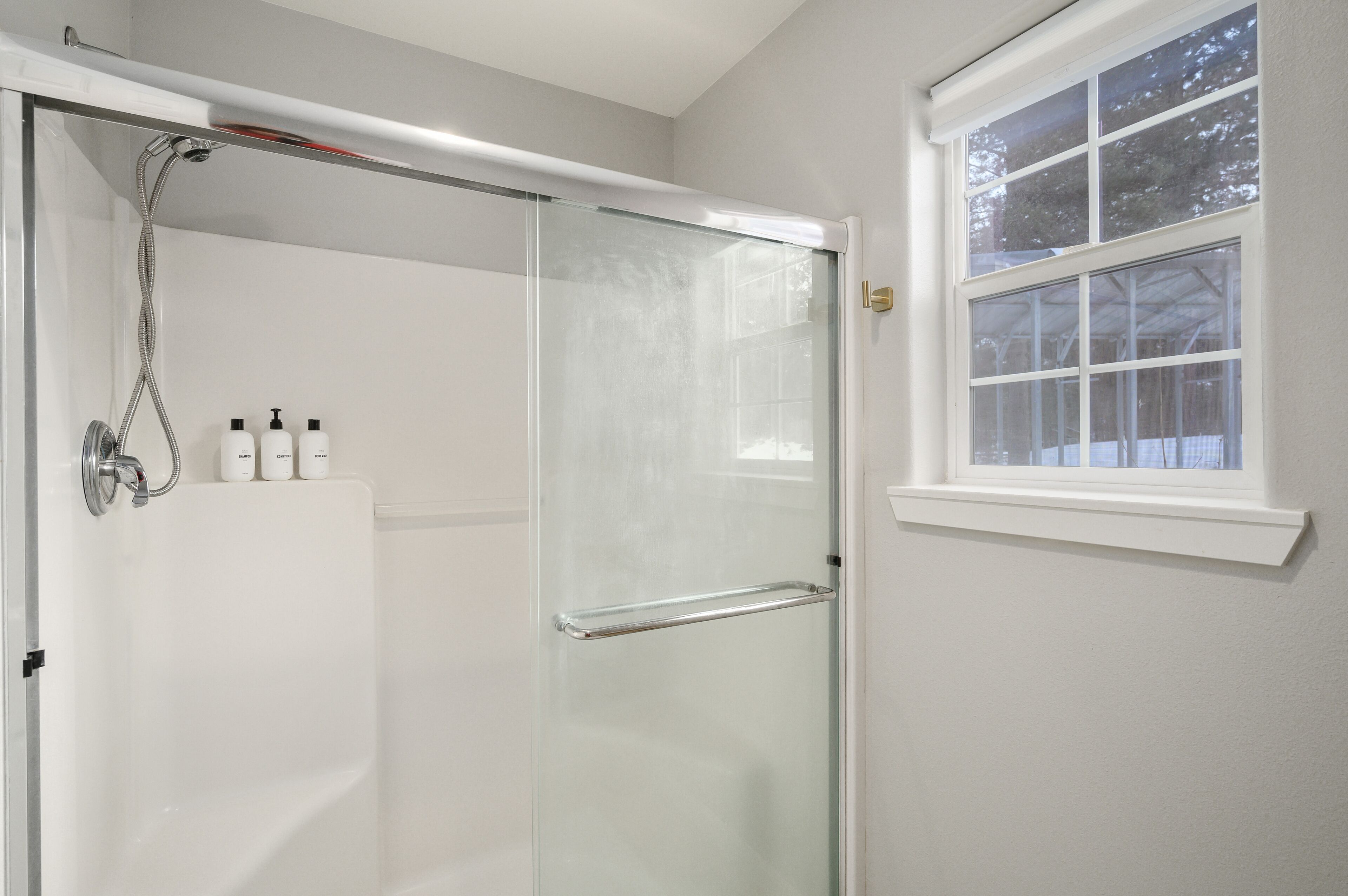 Une salle de bain moderne avec une douche à l’italienne en verre, une baignoire blanche et une fenêtre donnant sur la verdure.