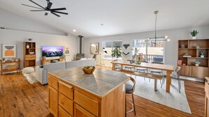 A spacious living area with a wooden dining table, a kitchen island, and a ceiling fan. - Bend Modern Cabin w/ Private Hot Tub . Fenced Yard, Game Room, Pet-Friendly (Bend)