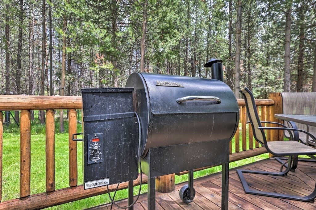 A portable grill on a wooden deck with a view of a forest.