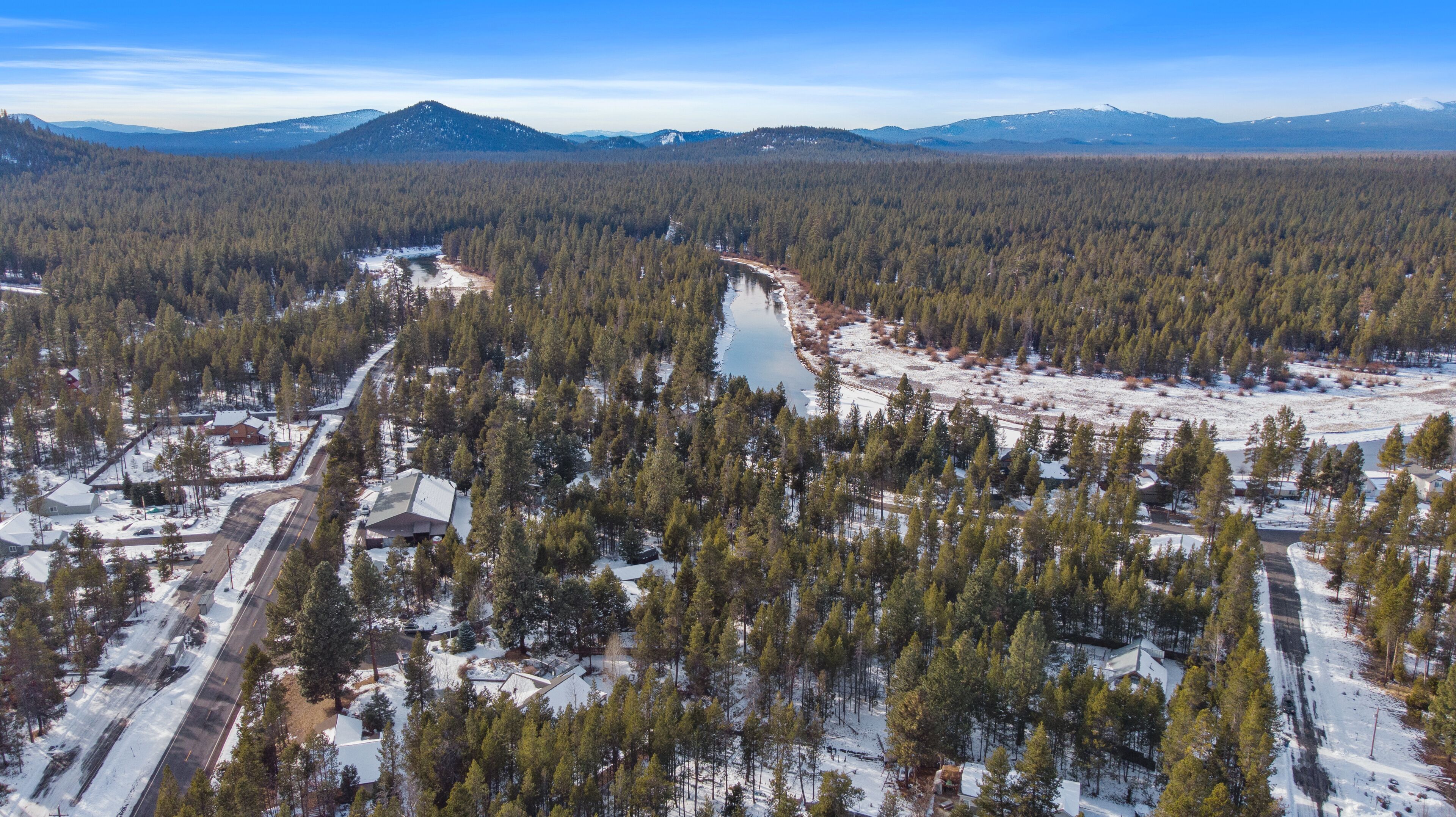 Ett flygbildsbild av ett skogsområde med en flod, hus och ett bergskedja i bakgrunden.