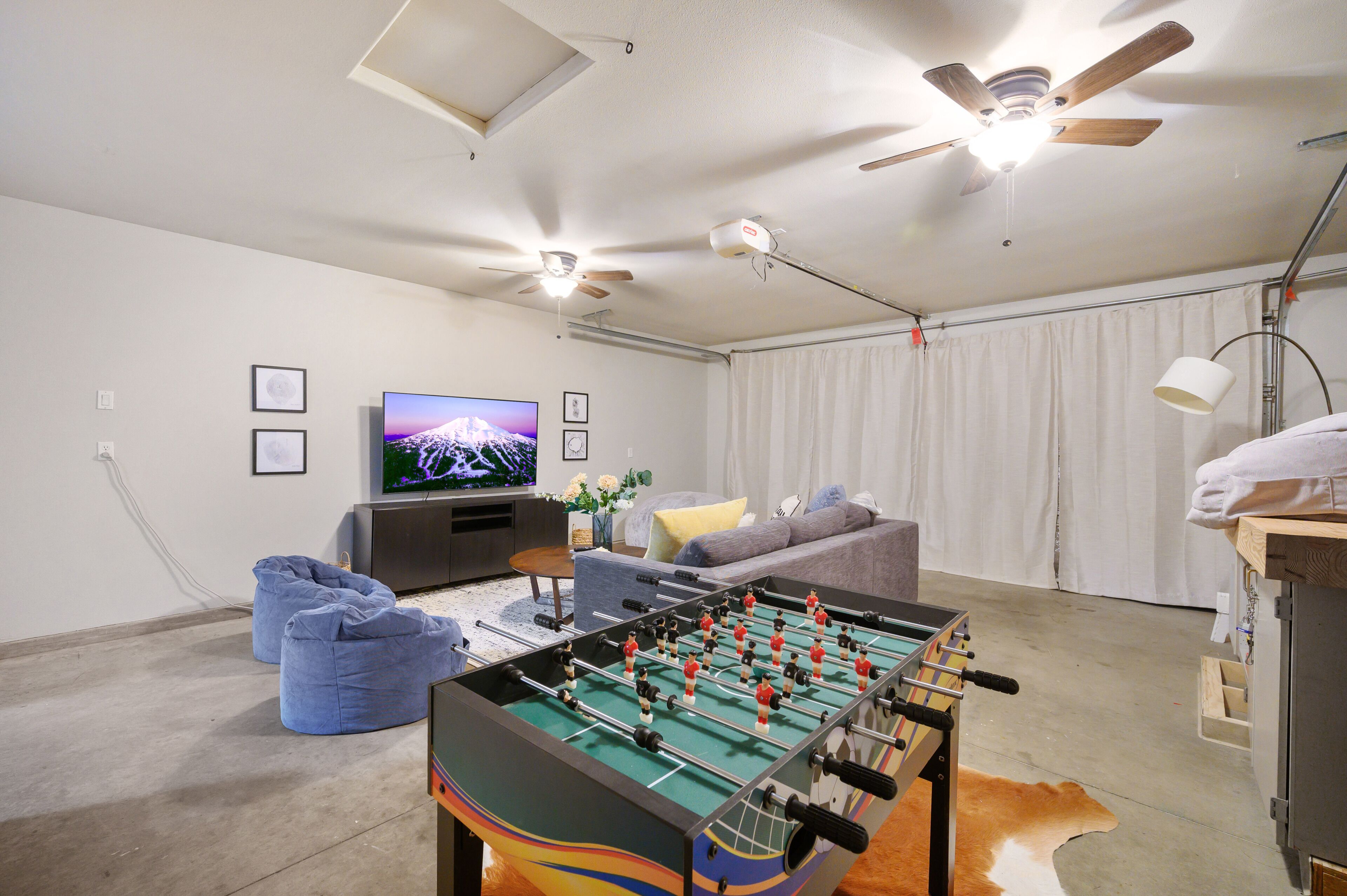 Una sala de estar con mesa de fútbol, televisor, ventilador de techo y sofá.