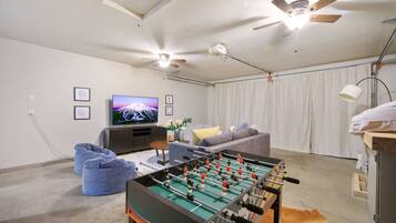 Una sala de estar con mesa de fútbol, televisor, ventilador de techo y sofá.