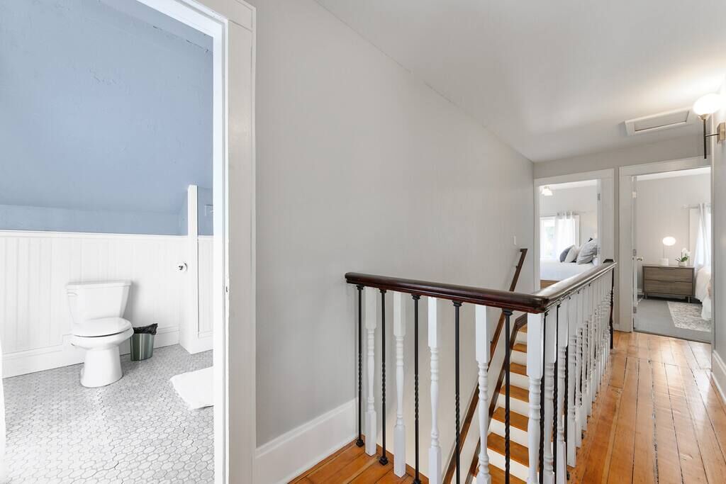 A hallway with a wooden floor, white walls, and a staircase with white balusters and a dark handrail.
