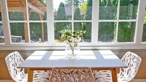 Comedor con mesa y dos sillas, un jarrón con flores y vistas amplias a través de grandes ventanales.