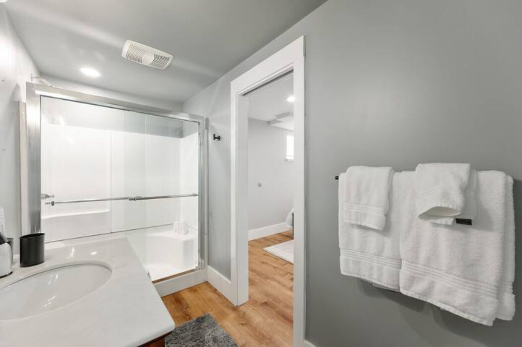 Een moderne badkamer met een douchecabine van glas, een wit wastafelmeubel en een handdoekrek met twee handdoeken.