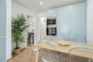 A modern kitchen with light blue cabinets, a built-in oven, and a dining area with a wooden table and clear chairs.