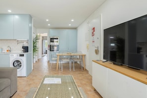 A compact kitchen with a washing machine, dining area with chairs, and a flat-screen TV on a wooden counter.