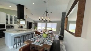 A modern kitchen with a central island, bar stools, and a dining area with a long table set for four. - Modern Key West look, Pool, Lake, Sleeps 10 (Punta Gorda)