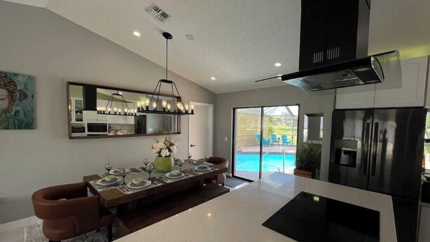 A modern kitchen with a central island, a dining area with a large mirror, and a view of a swimming pool. - Modern Key West look, Pool, Lake, Sleeps 10 (Punta Gorda)