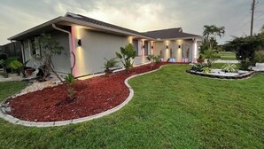 A two-story house with a well-maintained lawn and a variety of plants. - Modern Key West look, Pool, Lake, Sleeps 10 (Punta Gorda)