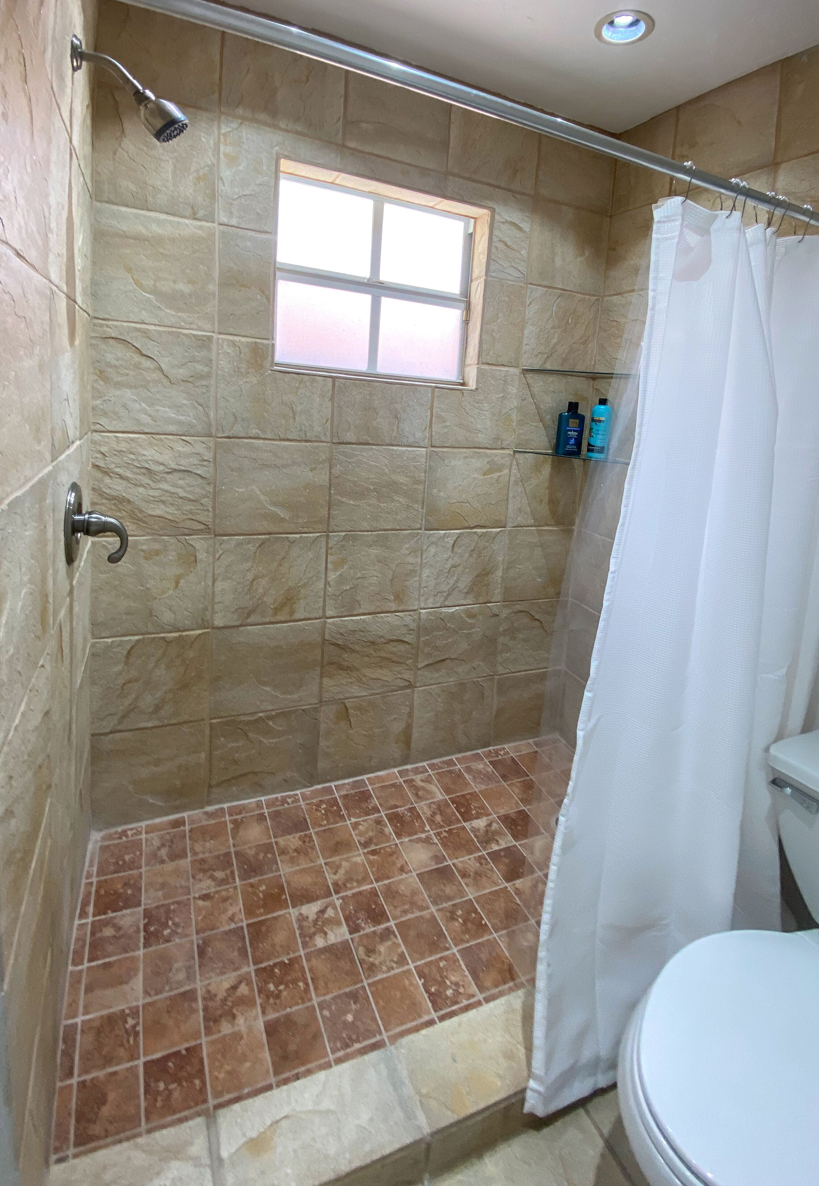A shower area with a window, a toilet, and a shower curtain.