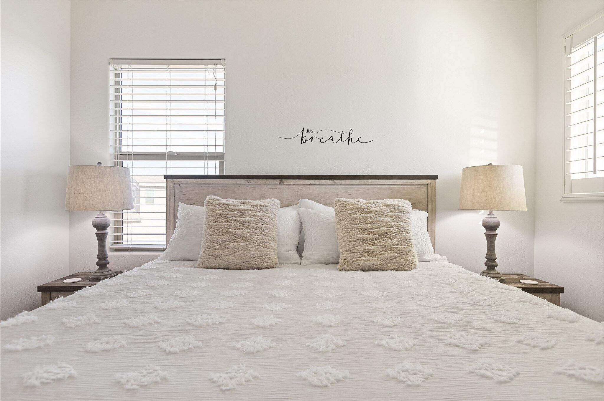 A bedroom with a large bed, two bedside lamps, and a wall-mounted sign that says "Just breathe".