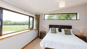 A bedroom with a large window, a bed with white bedding, two bedside tables, and a view of greenery outside.
