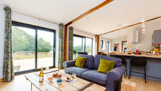 A modern living room with a sofa, a wooden coffee table, and a view of the outdoors through large windows.