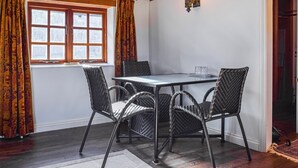 Ein Essbereich mit Tisch und vier Stühlen, einem Fenster mit Vorhängen und einer Wandleuchte.