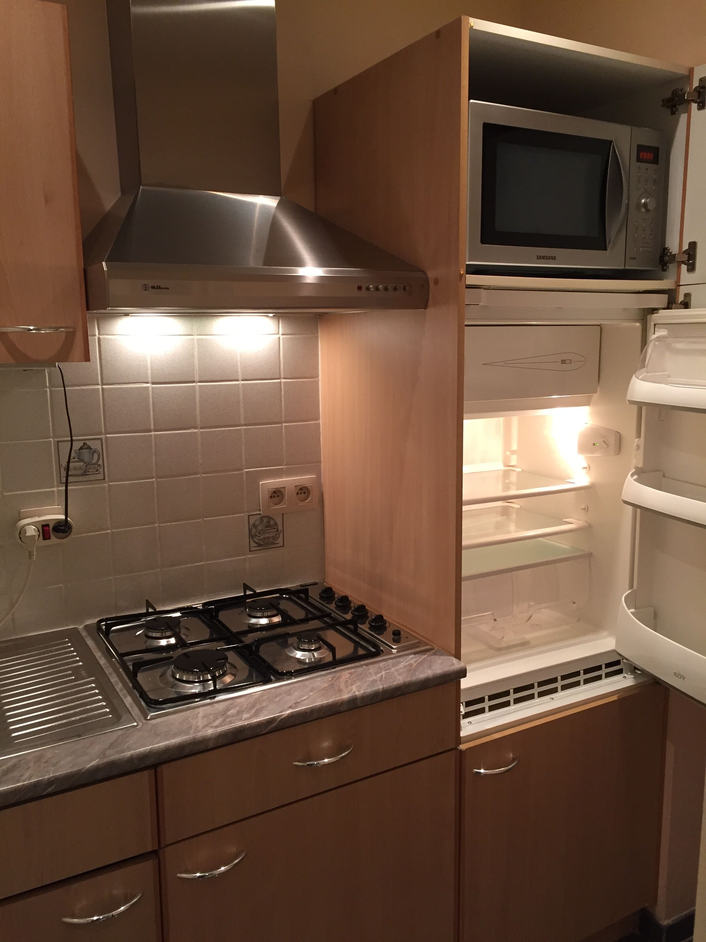 Een keuken met een gasfornuis, een roestvrijstalen afzuigkap, een magnetron en een inbouwkoelkast.